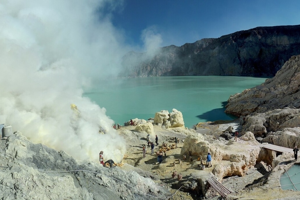 Het turquoise zure kratermeer van Kawah Ijen, met mijnwerkers die zwavel winnen tussen de rook.
