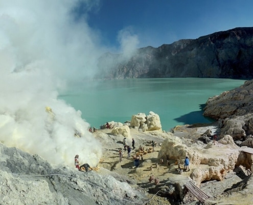 Het turquoise zure kratermeer van Kawah Ijen, met mijnwerkers die zwavel winnen tussen de rook.