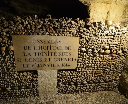 Een wand met menselijke botten en schedels in de Catacombes van Parijs, met een bordje dat de herkomst van de beenderen verme